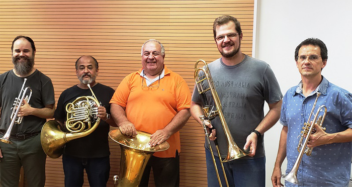 #OSUacessível Fotografia do Quinteto de Metais da Orquestra Sinfônica da Unicamp. Os músicos estão sorrindo e segurando seus instrumentos. Vestem roupas casuais.